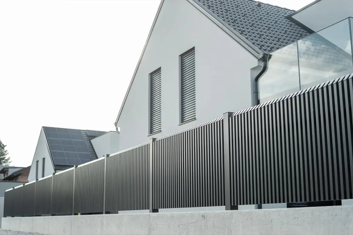Dunkelgrauer Aluminium-Lattenzaun vor einem weißen Wohnhaus